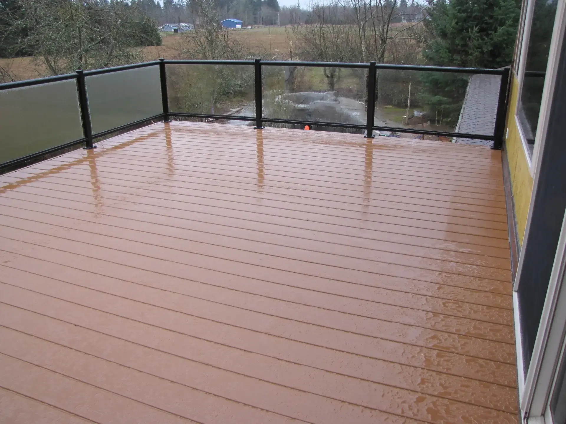 newly-cleaned-spacious-deck-with-glass-railings-on-the-residential-house-with-trees-and-houses-on-the-background-in-tacoma-wa
